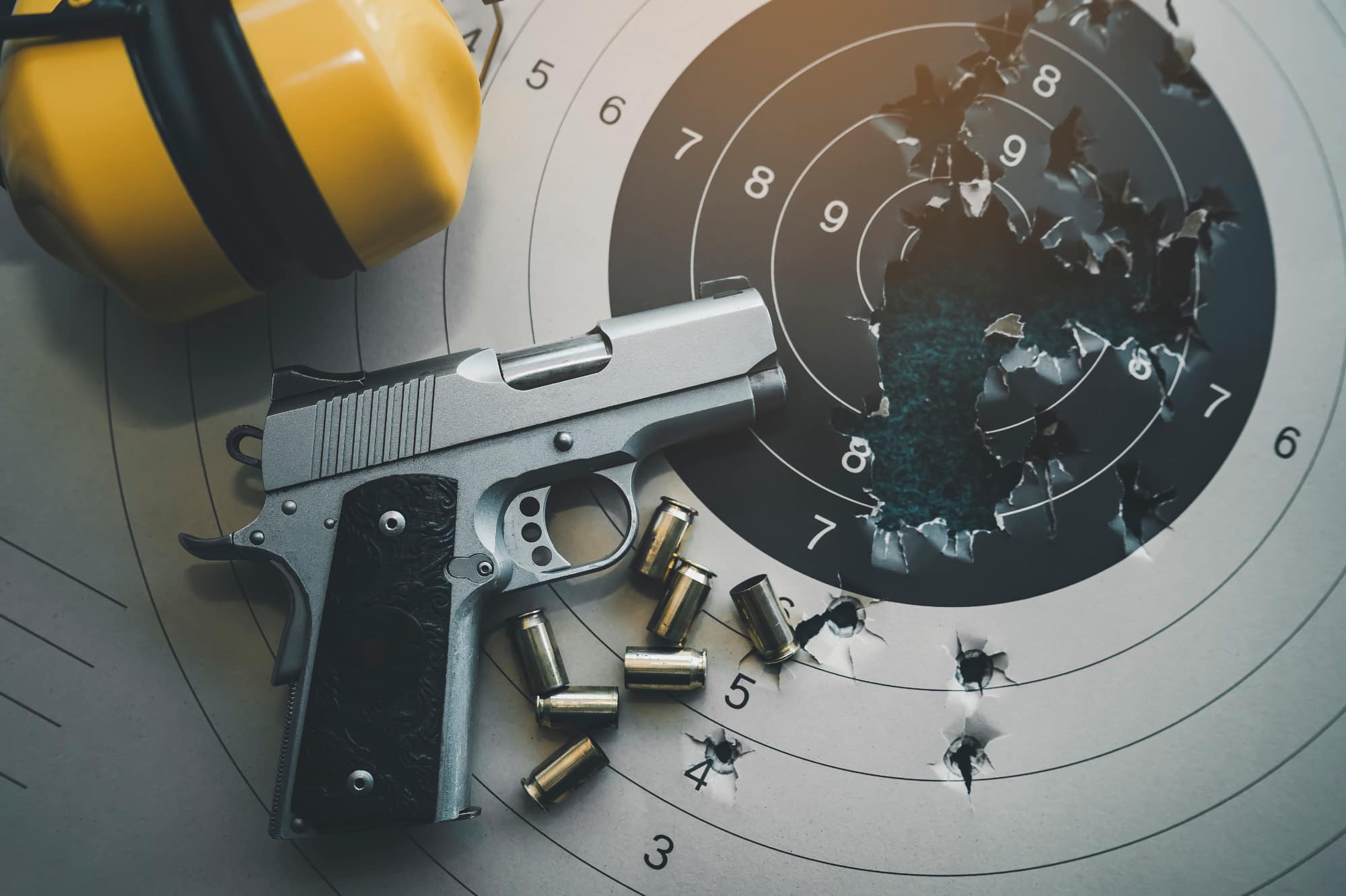 top view of handguns bullets and yellow headphones on used paper target
